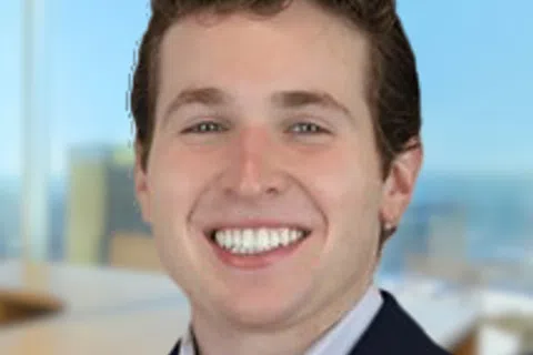 Smiling young man in business attire with light blue shirt and navy blazer in modern office interior.