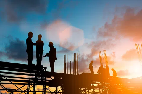 Silhouettes of construction workers on scaffolding during a colorful sunset sky at a building site.
