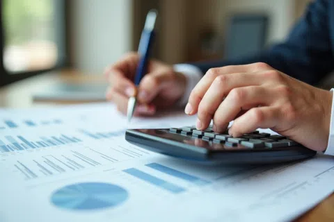 Person using calculator and analyzing financial charts and graphs on paper with pen in hand.