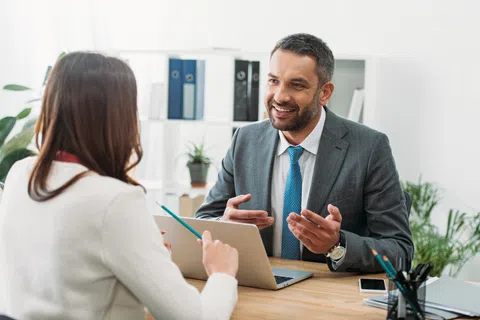 Businessman in a suit discussing with a woman at an office desk with laptop and documents