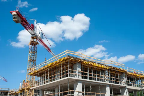Tower crane and concrete building under construction against a blue sky with white clouds.