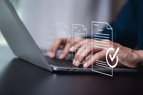Person typing on laptop with digital documents and checkmarks floating, symbolizing data verification or approval.