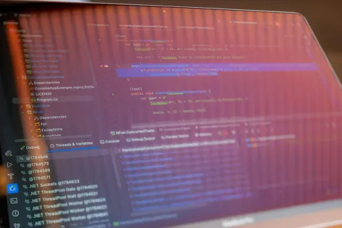 Laptop screen displaying colorful programming code and debugging interface with folder structure and variables panel.