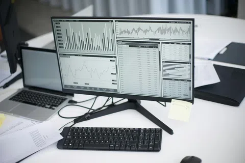 Computer monitor displaying various financial graphs and data charts on a clean office desk with keyboard