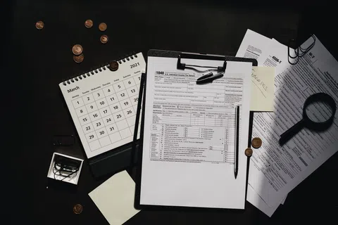 U.S. tax documents with pen, calendar showing March 2021, coins, paper clips, and magnifying glass on black surface