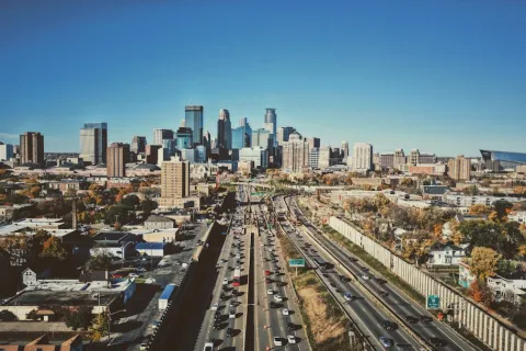 Aerial view of a busy highway leading into a city with skyscrapers under a clear blue sky.