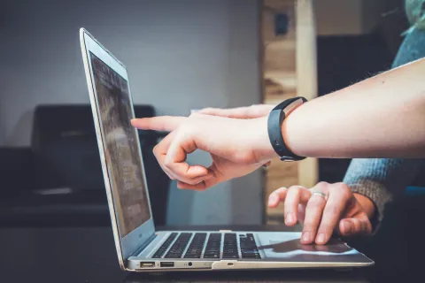 Managed IT services provider pointing at laptop screen while another uses the trackpad in a casual workspace setting