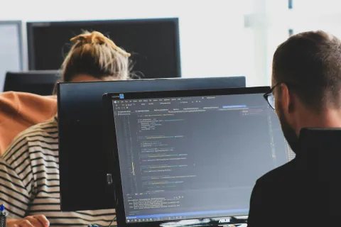 Two software developers working on coding displayed on a computer screen in a modern office environment.