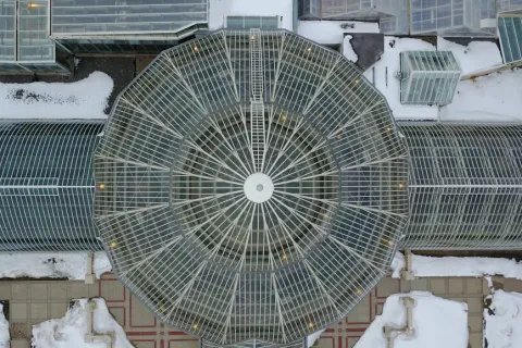 Aerial view of a large circular glass greenhouse structure with surrounding glass tunnels and snow-covered ground.