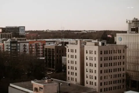 Urban cityscape featuring mid-rise buildings and rooftops under a pale sky during early evening.