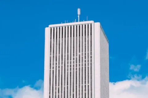 Tall white modern skyscraper with vertical window lines against a bright blue sky with a few clouds.