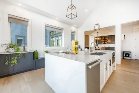 Bright modern kitchen with white marble island, dark cabinets, large windows, and hardwood floors.