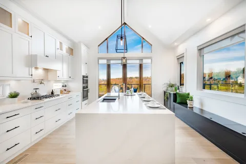 Bright modern kitchen with white cabinetry, large island, pendant lights, and expansive windows with outdoor views