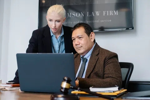 Two lawyers collaborating in an office with a laptop, legal documents, and a judge's gavel on the desk.