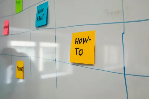 Sticky notes with words like HOW-TO and FUN FACT on a whiteboard with blue grid lines