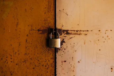 Rusty metal doors secured with a brass padlock in the center with weathered orange and beige paint.