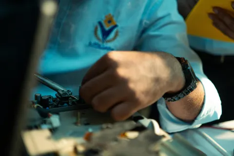 Close-up of a technician's hand repairing electronic equipment, wearing a blue uniform and black watch.