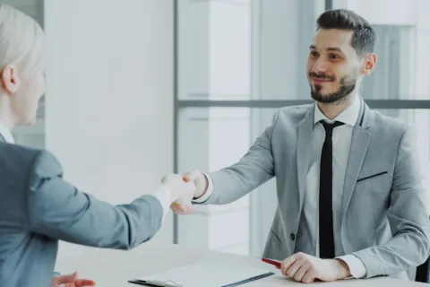 Two business professionals shaking hands during a meeting in a modern office setting.