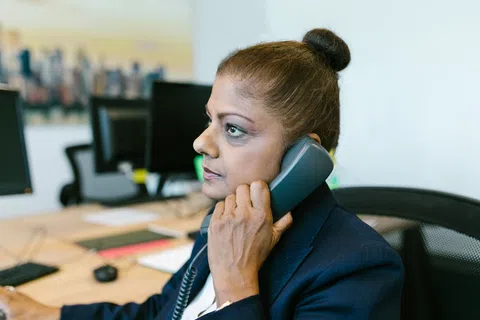 Professional woman in business attire talking on office phone at her desk with computer in background