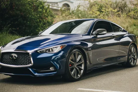 Blue Infiniti sports sedan parked outdoors near greenery and residential buildings under an overpass.