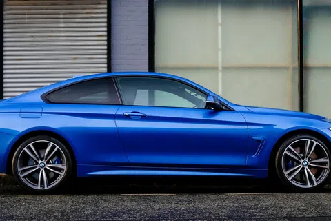 Sleek blue BMW coupe parked on street in front of gray brick building with 'Entrance' sign above door.