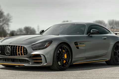 Sleek gray Mercedes AMG GT sports car with black and yellow accents parked on a road with blurred trees in background