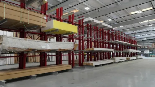 Interior of a large warehouse with red metal shelving holding various construction materials like wood and insulation.