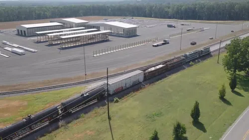 A freight train passes alongside a large lumberyard designed for engineered wood storage