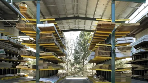 Stacks of lumber neatly arranged on racks under a covered outdoor storage area at a lumber yard.