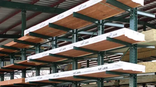 Stacks of lumber neatly arranged on racks under a covered outdoor storage area at a lumber yard.