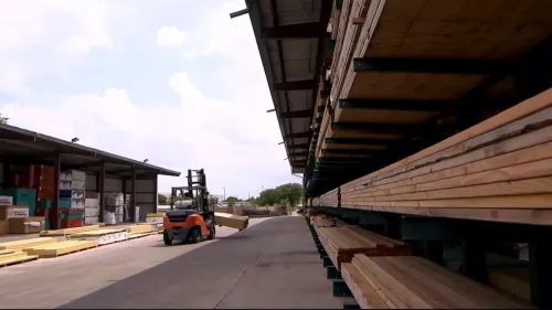 Stacks of lumber neatly arranged on racks under a covered outdoor storage area at a lumber yard.