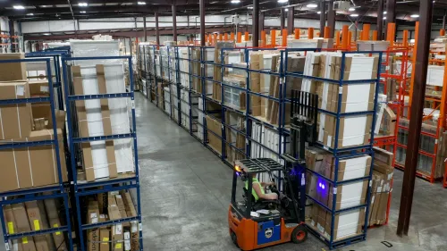 Forklift operating in large warehouse aisle with tall shelves packed with cardboard boxes and packages