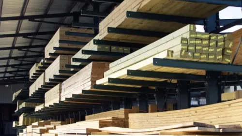 Stacks of lumber neatly arranged on racks under a covered outdoor storage area at a lumber yard.