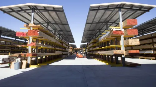 Stacks of lumber neatly arranged on racks under a covered outdoor storage area at a lumber yard.