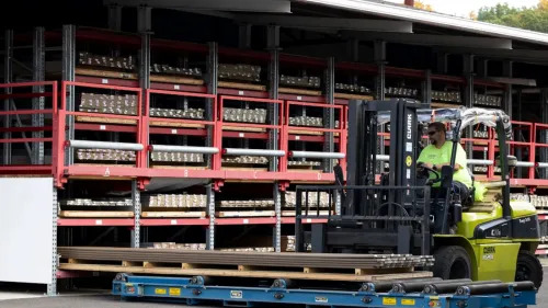 Stacks of lumber neatly arranged on racks under a covered outdoor storage area at a lumber yard.