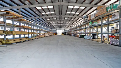 Large outdoor lumber yard with stacks of wooden planks organized on metal racks under a metal roof.