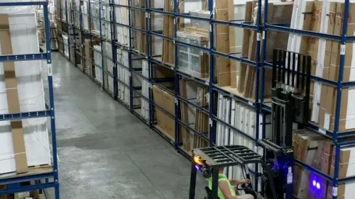Stacks of lumber neatly arranged on racks under a covered outdoor storage area at a lumber yard.