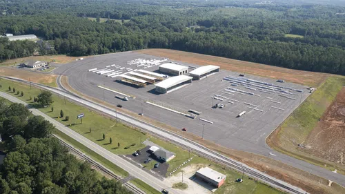 Aerial view of a large truck parking lot with trailers and loading docks surrounded by greenery and roads.