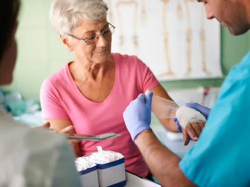 Senior woman receiving a wrist bandage from a healthcare professional in a medical clinic setting.