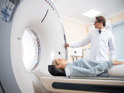 Patient lying on MRI scanner bed with technician operating the machine in a clinical setting.