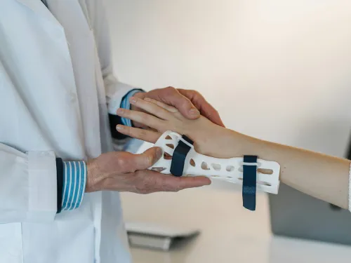 Doctor fitting a white wrist brace with blue straps on patient’s arm in a clinical setting.