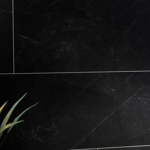 Close-up of black marble tiles with white veining and thin grout lines, next to green plant leaves.