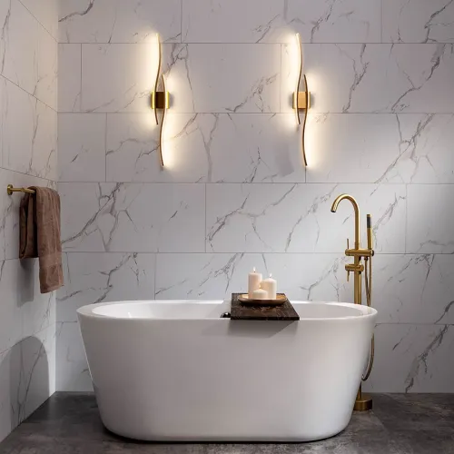 Modern bathroom with freestanding white bathtub, gold faucet, marble wall tiles, and ambient wall lights.