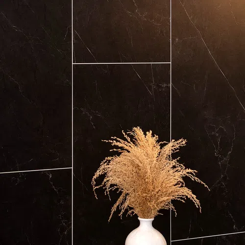 White vase with dried beige pampas grass against a black marble tile wall with white grout lines.