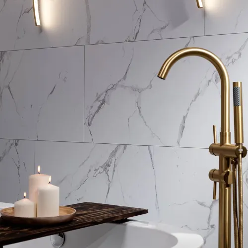 Modern bathroom with marble wall tiles, gold faucet, bathtub, and three lit white candles on wooden tray.