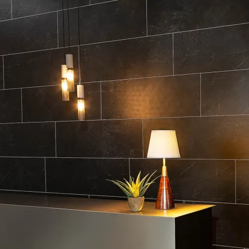 Modern interior with black tiled wall, hanging pendant lights, a table lamp, and a small potted plant on a sleek surface.