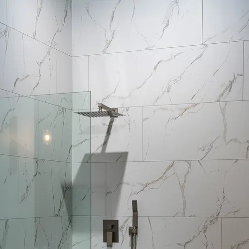 Modern walk-in shower with large rain showerhead and white marble wall tiles with gray veining.