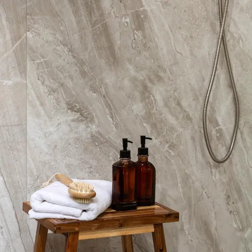 Wooden bench in bathroom holds white towels, wooden hairbrush, and amber soap dispensers against stone wall with shower hose.