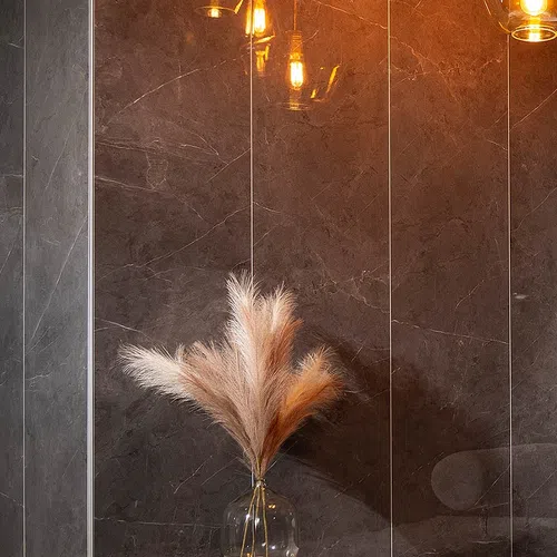 Decorative pampas grass in a glass vase against a dark marble wall with warm hanging lights.