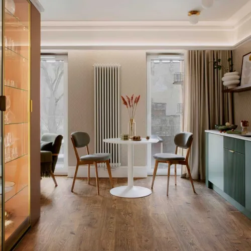 Cozy modern dining area with round white table, two gray chairs, wood flooring, and natural light from tall windows.